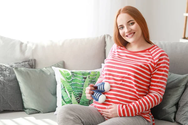 Beautiful pregnant woman with baby booties at home — Stock Photo, Image