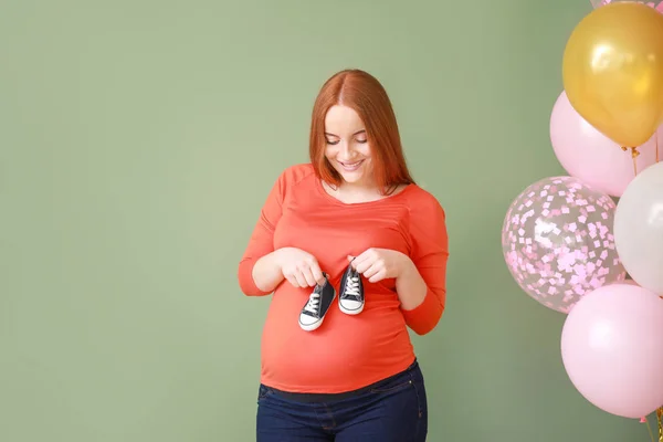 Beautiful pregnant woman with baby booties and air balloons on color background — Stock Photo, Image