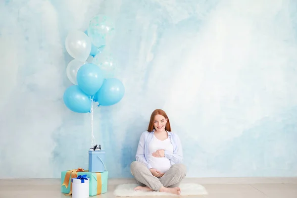 Femeie gravidă frumoasă cu cadouri de duș pentru copii lângă peretele color — Fotografie, imagine de stoc