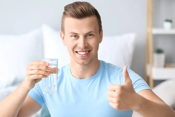 Knappe man met glas water weergegeven duim-up thuis — Stockfoto