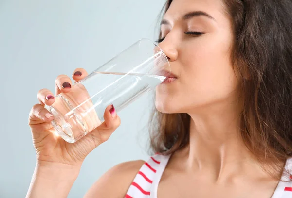 Mooie jonge vrouw drinken water op licht achtergrond — Stockfoto