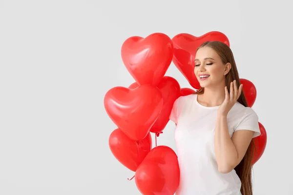 Hermosa mujer joven con globos de aire en forma de corazón sobre fondo claro — Foto de Stock