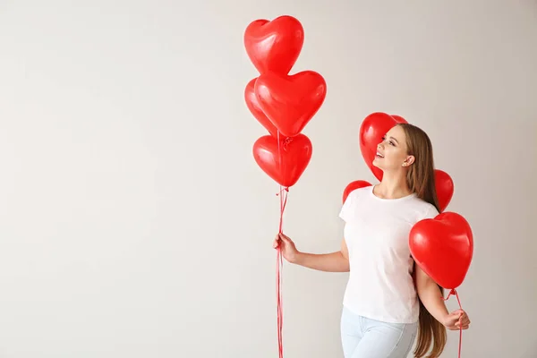 Beautiful young woman with heart-shaped air balloons on light background — Stock Photo, Image