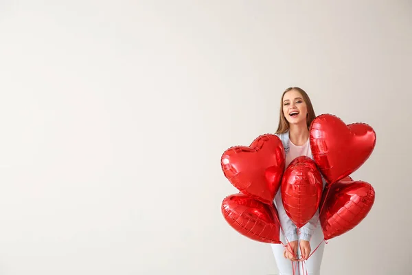 Hermosa mujer joven con globos de aire en forma de corazón sobre fondo claro —  Fotos de Stock
