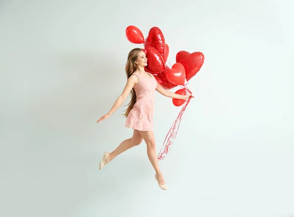 Mulher jovem despreocupada bonita com balões de ar em forma de coração perto da parede de luz — Fotografia de Stock