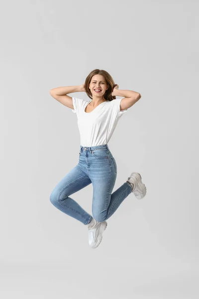 Skákání mladé ženy v džínách na bílém pozadí — Stock fotografie