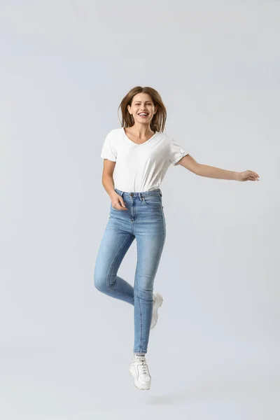 Mujer joven saltando en jeans sobre fondo blanco —  Fotos de Stock