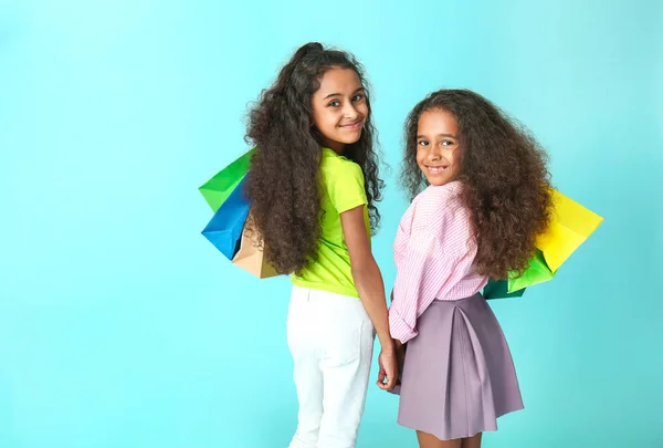 Schattige Afro-Amerikaanse meisjes met boodschappentassen op kleur achtergrond — Stockfoto