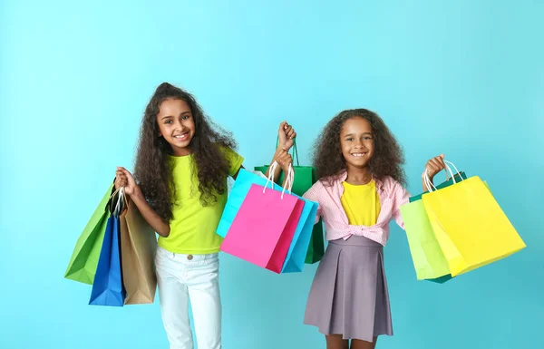 Χαριτωμένα αφροαμερικάνικα κορίτσια με σακούλες για ψώνια στο χρώμα φόντο — Φωτογραφία Αρχείου