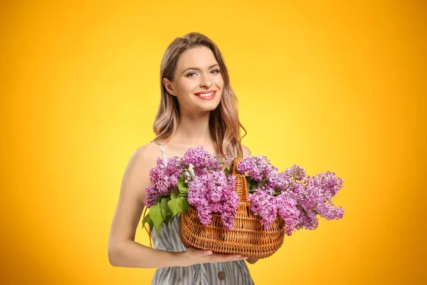 Beautiful young woman with bouquet of lilac flowers in basket on color background — Stock Photo, Image