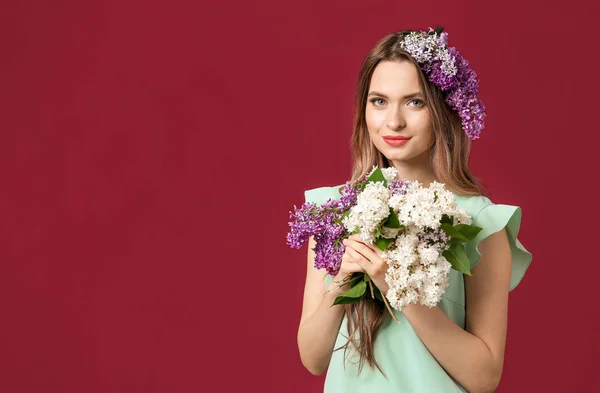 Beautiful young woman with lilac flowers on color background — Stok fotoğraf