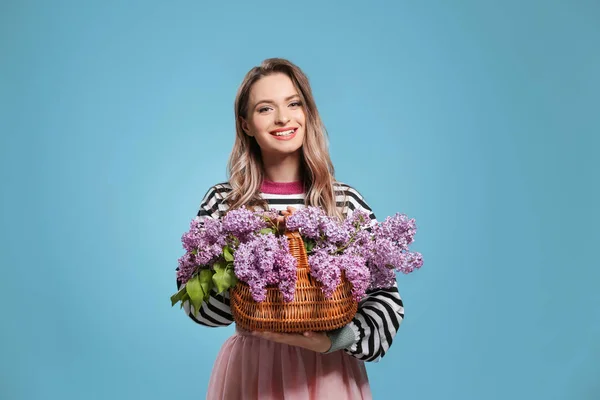 Όμορφη νεαρή γυναίκα με μπουκέτο πασχαλιά λουλούδια στο καλάθι στο χρώμα φόντο — Φωτογραφία Αρχείου