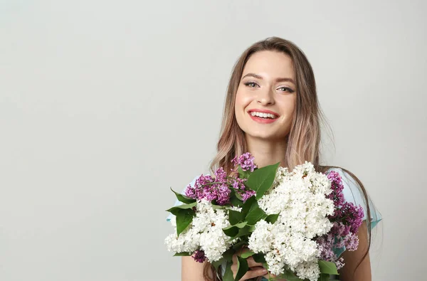 光の背景にライラックの花を持つ美しい若い女性 — ストック写真