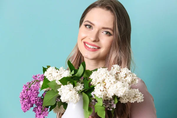 Krásná mladá žena s kyticí fialovými květy na barevném pozadí — Stock fotografie