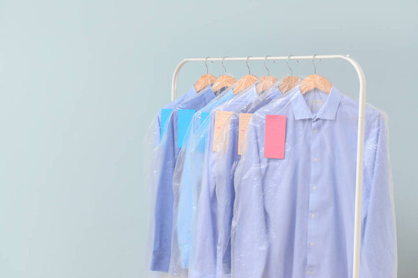 Rack with clothes after dry-cleaning on light background
