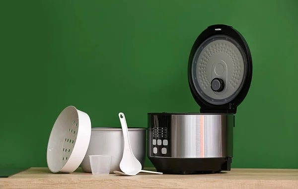 Modern multi cooker with accessories on table against color background — Stock Photo, Image
