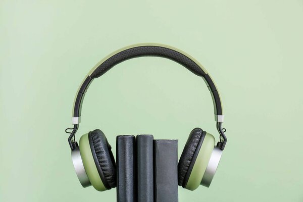 Books and modern headphones on color background. Concept of audiobook