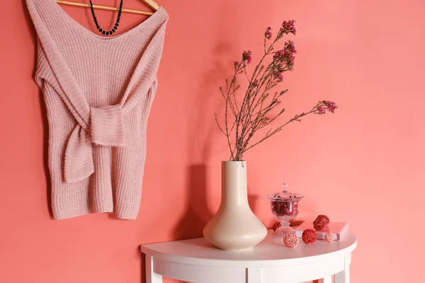 Mesa con decoración y ropa femenina colgando en la pared de color en la habitación — Foto de Stock