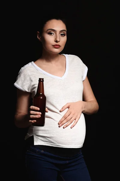 Těhotná žena s lahví piva na tmavém pozadí — Stock fotografie