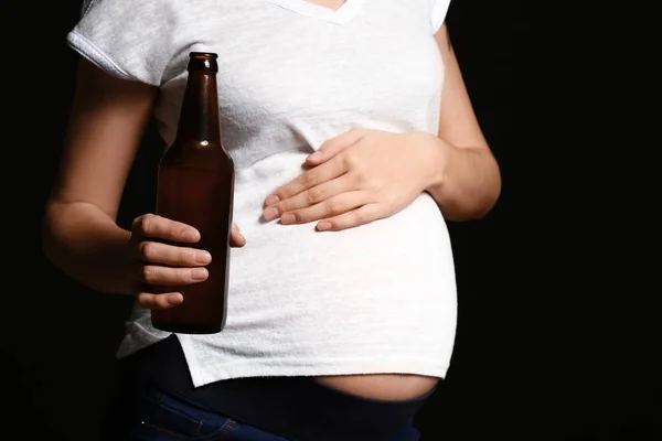 Mulher grávida com garrafa de cerveja no fundo escuro — Fotografia de Stock