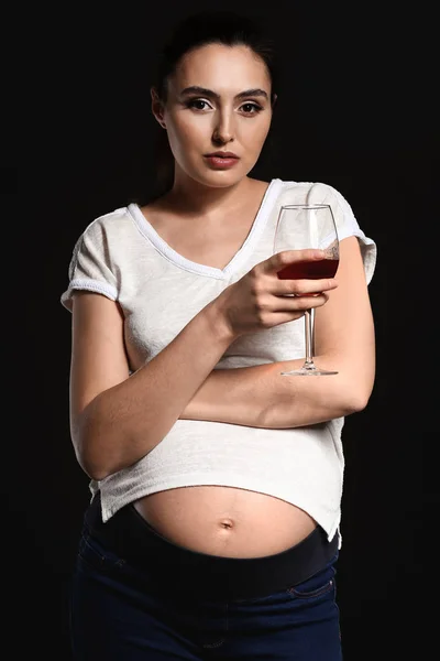 Mulher grávida com copo de álcool no fundo escuro — Fotografia de Stock