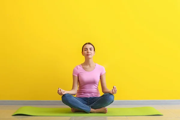 Mulher bonita praticando ioga perto da parede de cor — Fotografia de Stock