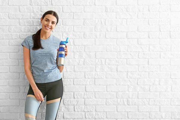 Αθλητική γυναίκα με μπουκάλι νερό κοντά σε τοίχο τούβλο — Φωτογραφία Αρχείου