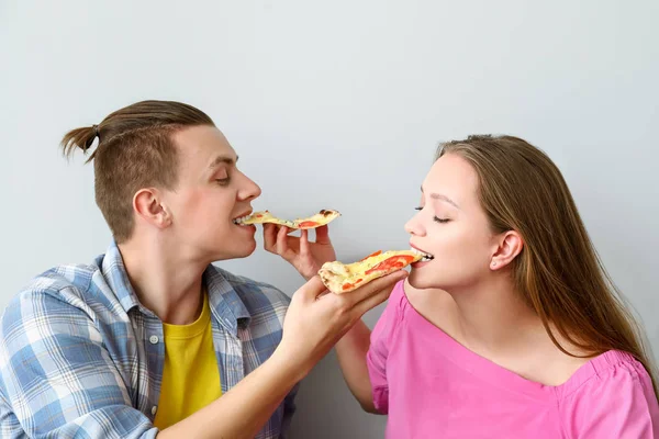 Young couple eating tasty pizza on light background — Stock Photo, Image