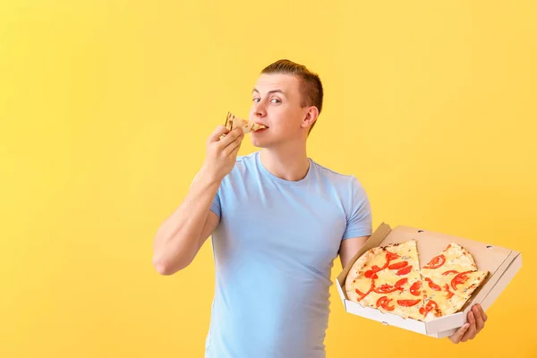 Handsome man eating tasty pizza on color background — Stock Photo, Image