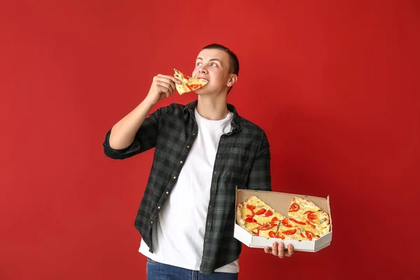 Красивый человек ест вкусную пиццу на цветном фоне — стоковое фото