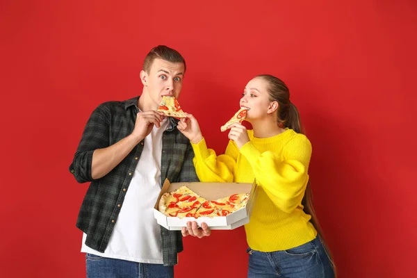 一对年轻夫妇在彩色背景下吃着美味的披萨 — 图库照片