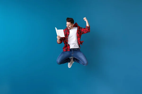 Saltando joven con libro sobre fondo de color — Foto de Stock