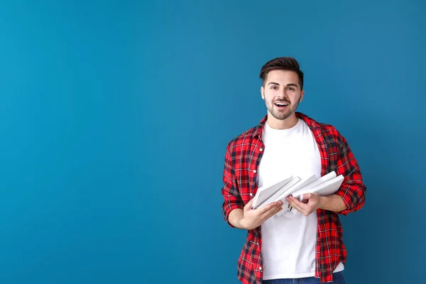 Excited young man with books on color background — Stock Photo, Image