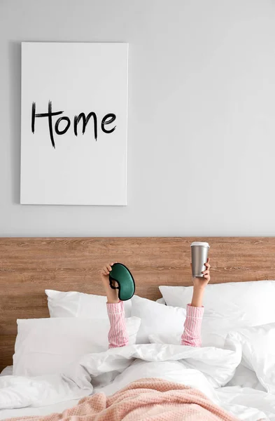 Jeune femme avec tasse de café chaud et masque de sommeil couché au lit — Photo