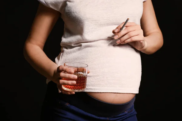 Mulher grávida com copo de álcool e cigarro em fundo escuro — Fotografia de Stock