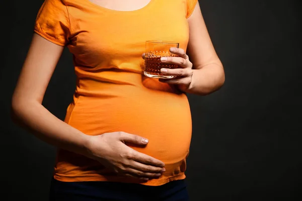 Mulher grávida com copo de álcool no fundo escuro — Fotografia de Stock