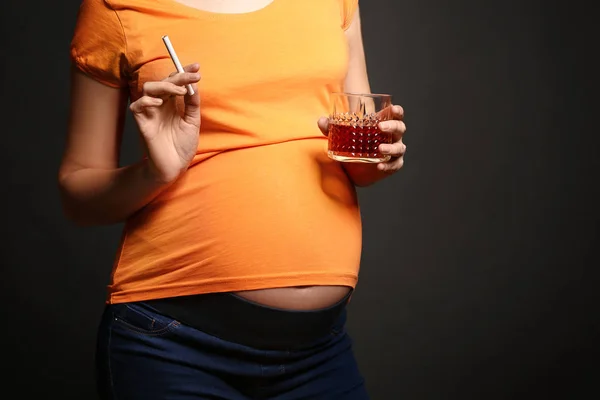 Mulher grávida com copo de álcool e cigarro em fundo escuro — Fotografia de Stock