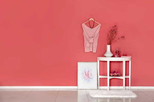 Τραπέζι με διακόσμηση και γυναικεία ρούχα κρέμονται στο χρώμα τοίχου στο δωμάτιο — Φωτογραφία Αρχείου