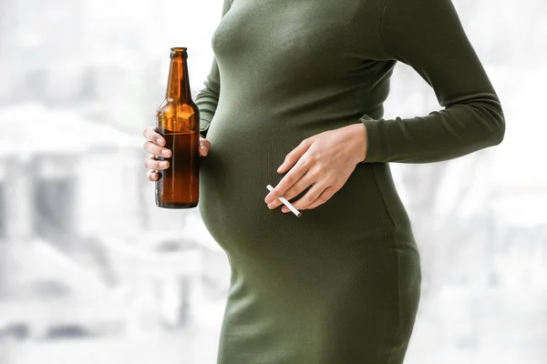 Mulher grávida com cerveja e cigarro perto da janela — Fotografia de Stock