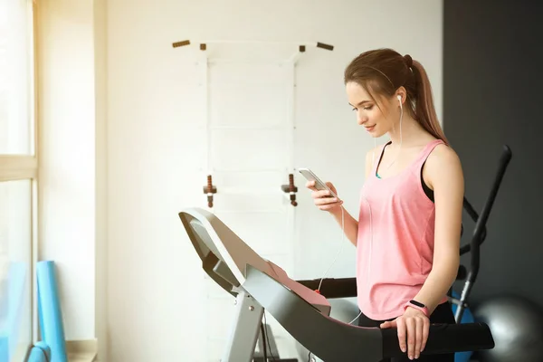 Sporty young woman listening to music while training on treadmill in gym — Stock Photo, Image