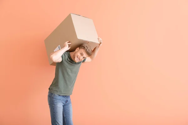 Renkli arka planda ağır karton kutu ile genç adam — Stok fotoğraf