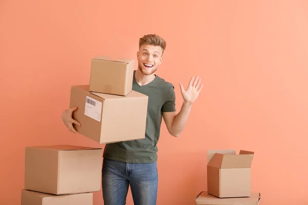 Young man with cardboard boxes on color background — Stok fotoğraf