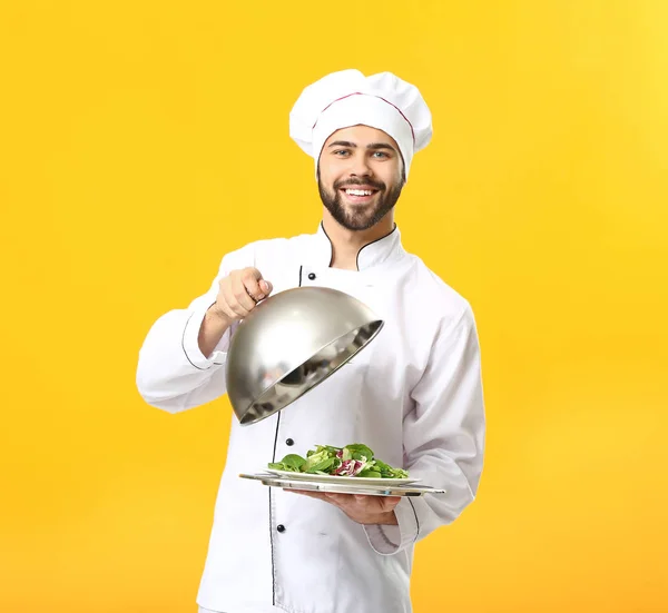 Schöner männlicher Koch mit Salat auf farbigem Hintergrund — Stockfoto