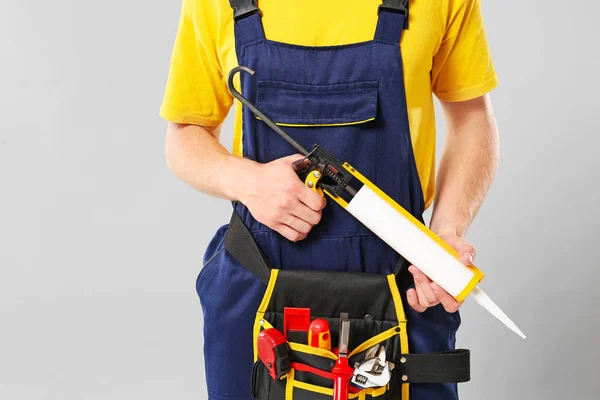 Plumber with tools belt and sealant on grey background — Stock Photo, Image
