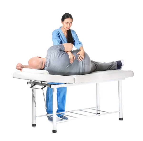 Jovem fisioterapeuta asiático trabalhando com o homem sênior em fundo branco — Fotografia de Stock