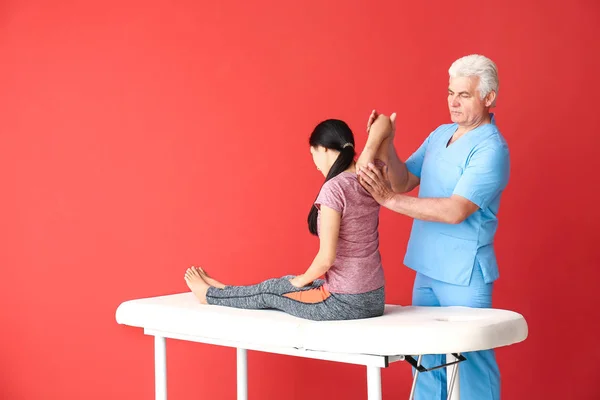 Maduro fisioterapeuta trabalhando com jovem mulher asiática em fundo de cor — Fotografia de Stock