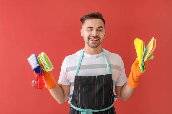 Happy young man with cleaning supplies on color background — Stock Photo, Image