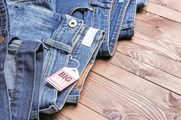 Calça jeans elegante com tag "VENDA GRANDE" no fundo de madeira, close-up — Fotografia de Stock