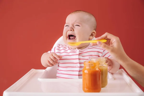 Pleurer petit bébé manger de la nourriture sur fond de couleur — Photo