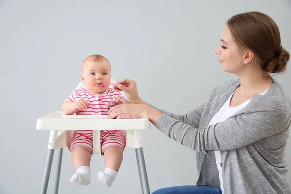 Mother feeding her little baby on grey background — Stock Photo, Image